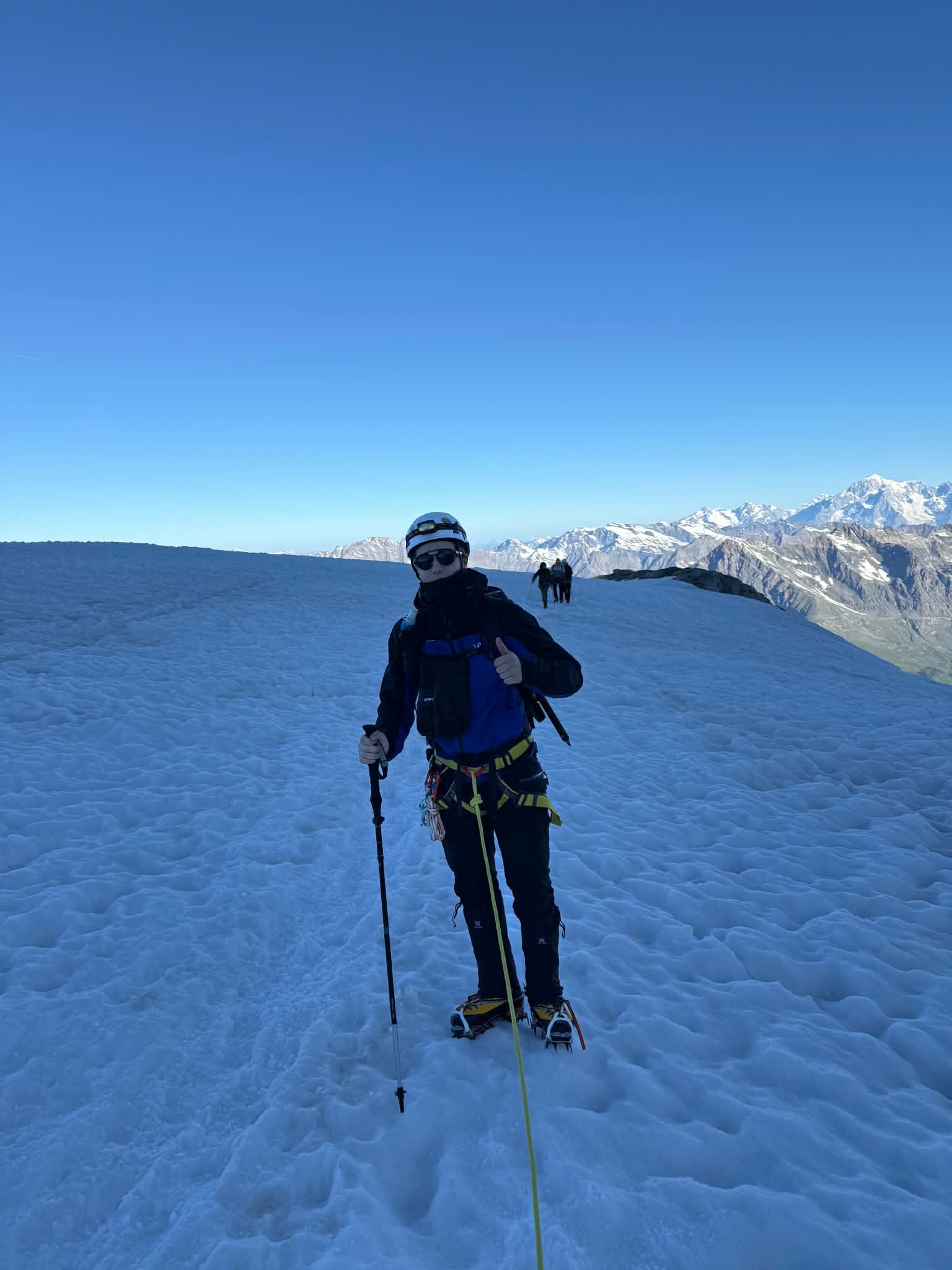 Frank Andrew Annion roped up on a glacier with crampons and a trekking pole, snow-capped peaks behind him